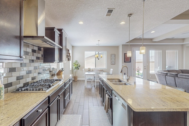 kitchen with tasteful backsplash, stainless steel appliances, light wood-type flooring, wall chimney range hood, and a sink