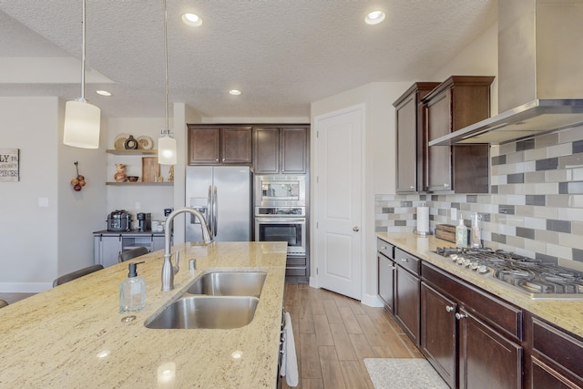 kitchen featuring stainless steel appliances, a sink, hanging light fixtures, decorative backsplash, and wall chimney exhaust hood