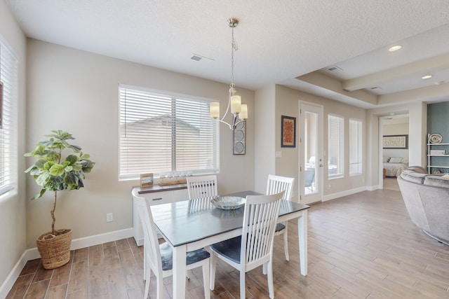 dining space with light wood finished floors, baseboards, a raised ceiling, and a textured ceiling