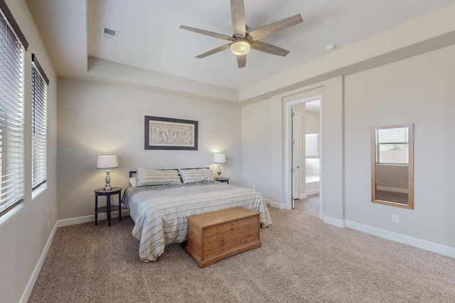 carpeted bedroom with a ceiling fan, a raised ceiling, visible vents, and baseboards