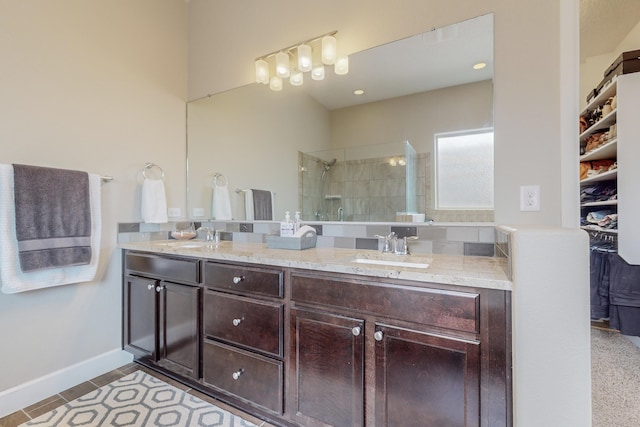 bathroom featuring tile patterned flooring, a sink, baseboards, a tile shower, and double vanity