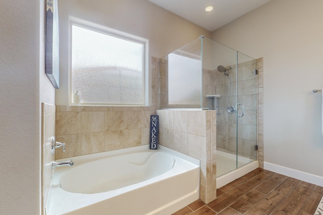 bathroom with a stall shower, baseboards, a bath, and wood finish floors