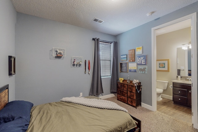 bedroom with baseboards, visible vents, connected bathroom, light colored carpet, and a textured ceiling