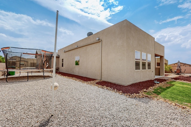 view of side of property with a trampoline and stucco siding