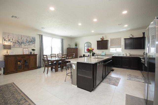 kitchen featuring a kitchen breakfast bar, dishwasher, an island with sink, light stone counters, and sink