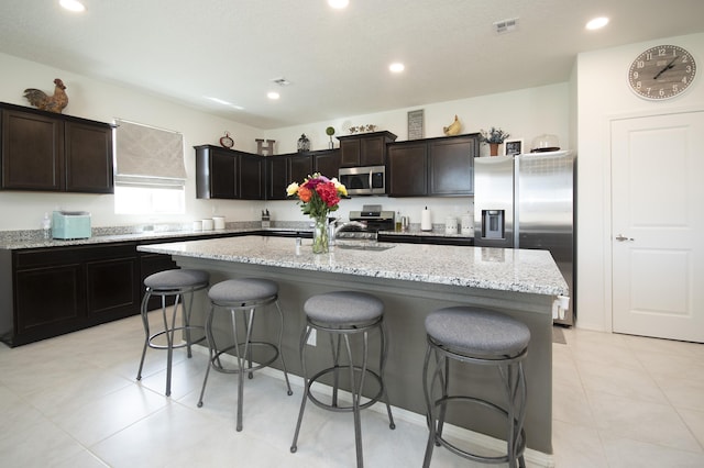 kitchen with stainless steel appliances, light stone counters, a breakfast bar, a kitchen island, and sink