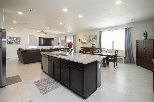 kitchen with an island with sink, stainless steel appliances, light stone countertops, sink, and a textured ceiling