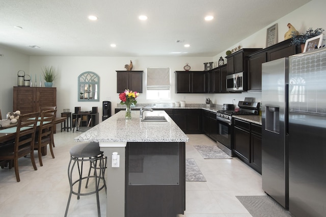 kitchen featuring appliances with stainless steel finishes, sink, a kitchen breakfast bar, an island with sink, and light stone countertops