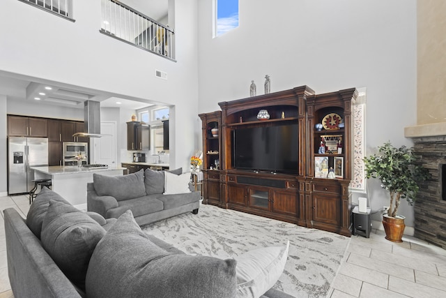 tiled living room featuring a high ceiling and a stone fireplace