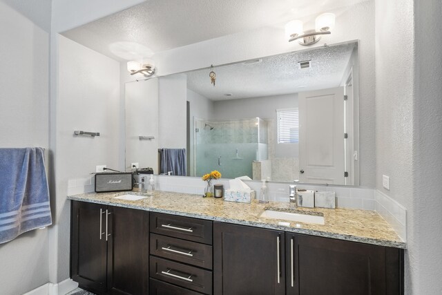 bathroom with vanity, a shower with shower door, and a textured ceiling