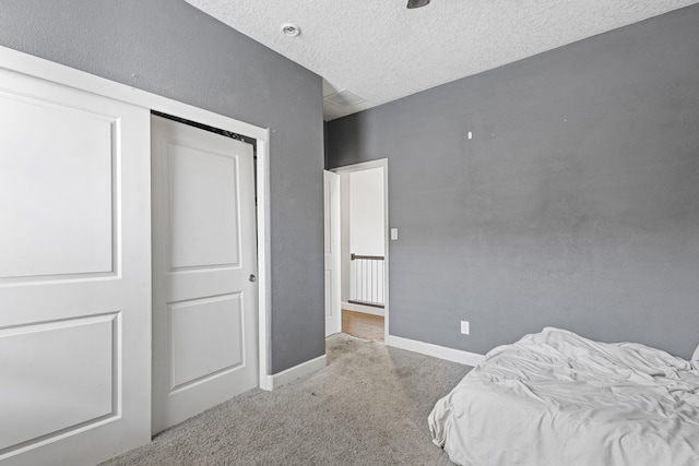 bedroom with a textured ceiling, light colored carpet, and a closet