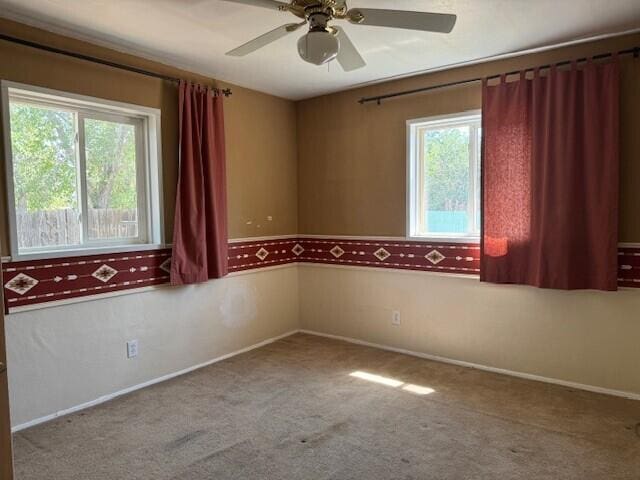 carpeted empty room featuring a healthy amount of sunlight, ceiling fan, and baseboards