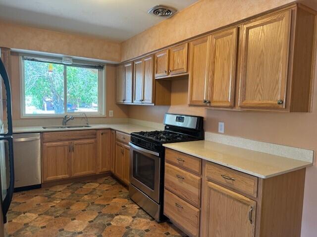 kitchen with stainless steel appliances, a sink, visible vents, light countertops, and brown cabinets