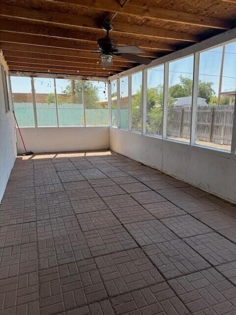 unfurnished sunroom featuring beam ceiling and a ceiling fan