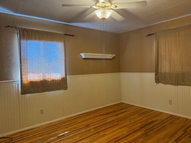 unfurnished room with ceiling fan, wainscoting, and wood finished floors