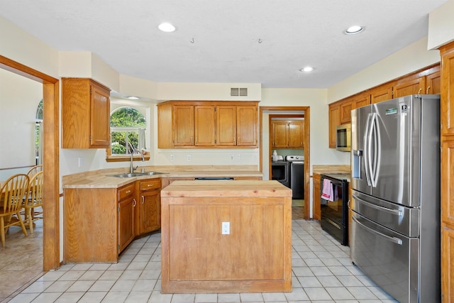 kitchen featuring appliances with stainless steel finishes, independent washer and dryer, a center island, light tile patterned floors, and sink