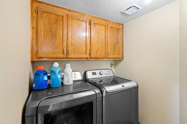 clothes washing area with cabinets, separate washer and dryer, and a textured ceiling