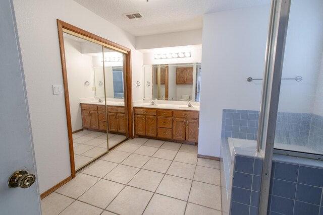 bathroom with tiled bath, tile patterned floors, a textured ceiling, and vanity