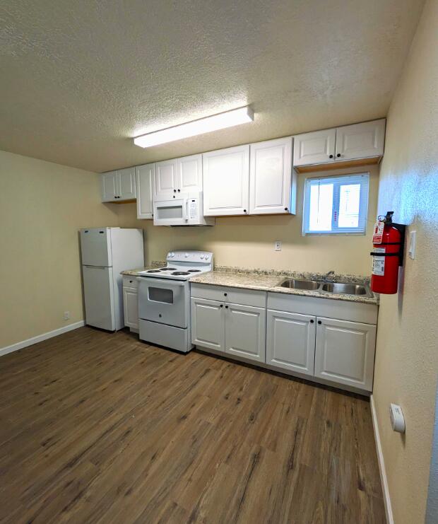 kitchen featuring white cabinetry, white appliances, a textured ceiling, dark wood-type flooring, and sink