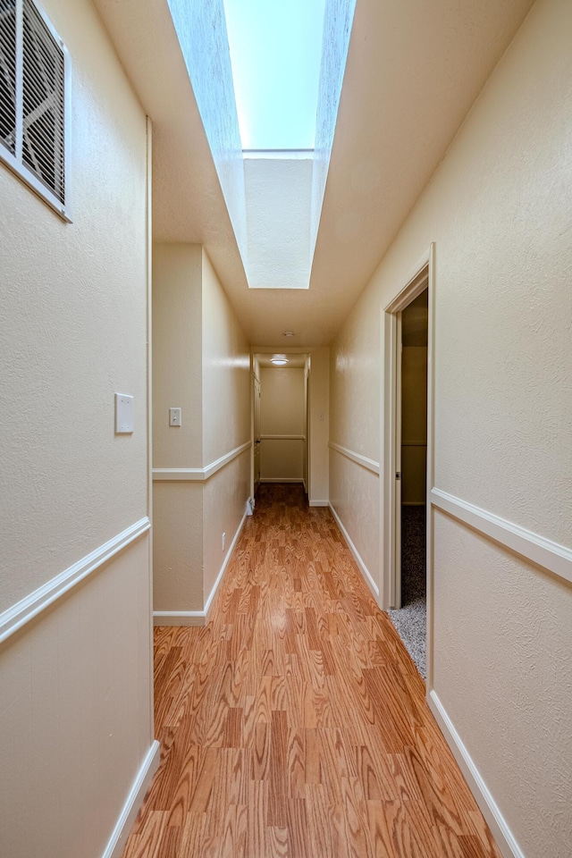 corridor with light wood-type flooring and a skylight