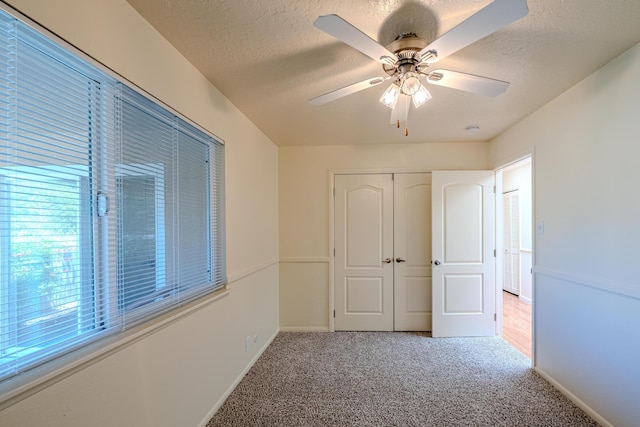 unfurnished bedroom featuring ceiling fan, carpet floors, multiple windows, a textured ceiling, and a closet