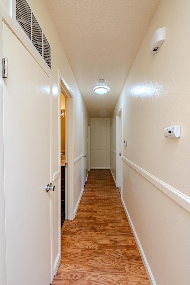 hallway with a textured ceiling and light wood-type flooring