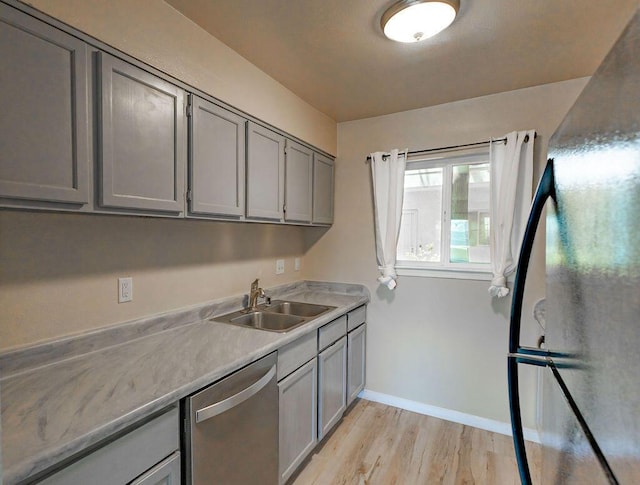 kitchen with stainless steel dishwasher, gray cabinets, sink, and light wood-type flooring