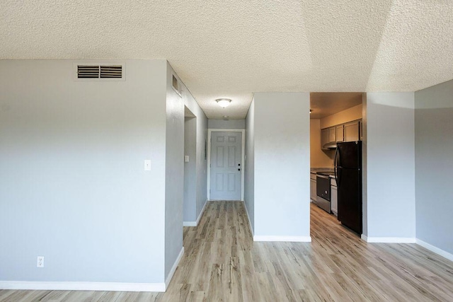 kitchen with black fridge, stainless steel range with electric cooktop, a textured ceiling, and light wood-type flooring