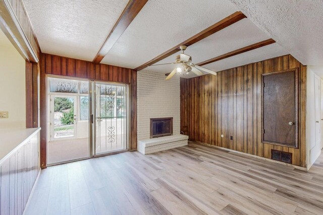 unfurnished living room featuring brick wall, a fireplace, a textured ceiling, and beam ceiling