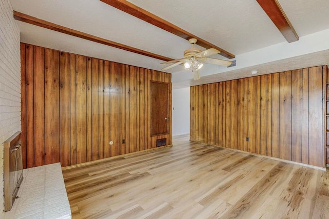 empty room featuring beamed ceiling, wood walls, ceiling fan, and light wood-type flooring