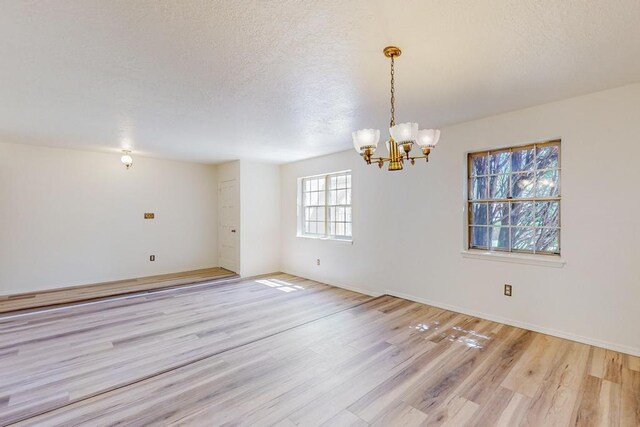 unfurnished room featuring an inviting chandelier, light wood-type flooring, and a textured ceiling