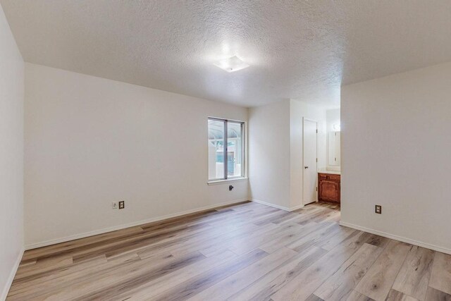 empty room with light wood-type flooring and a textured ceiling