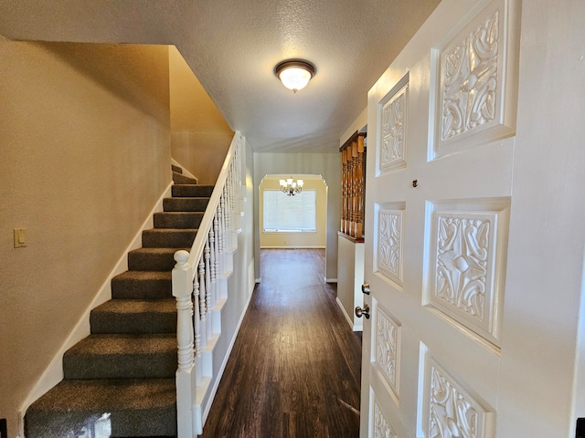 stairs with a notable chandelier, a textured ceiling, and dark wood-type flooring