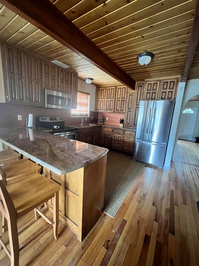 kitchen featuring tasteful backsplash, light wood-type flooring, beamed ceiling, appliances with stainless steel finishes, and sink