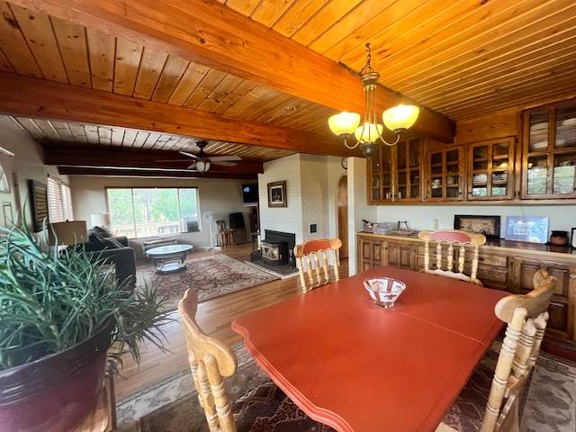 dining space featuring ceiling fan with notable chandelier, a large fireplace, beam ceiling, wooden ceiling, and hardwood / wood-style flooring