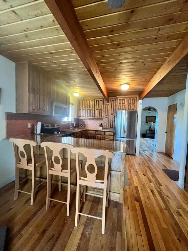 kitchen with light hardwood / wood-style flooring, stainless steel refrigerator, a kitchen bar, and kitchen peninsula