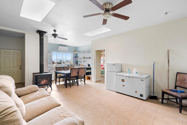 living room featuring ceiling fan, a wood stove, a skylight, a wall mounted AC, and light tile patterned floors