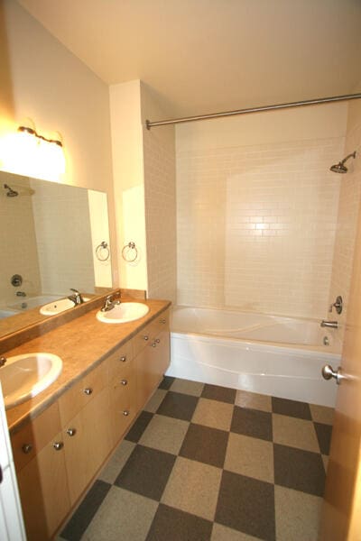 bathroom featuring tiled shower / bath, tile patterned flooring, and dual bowl vanity