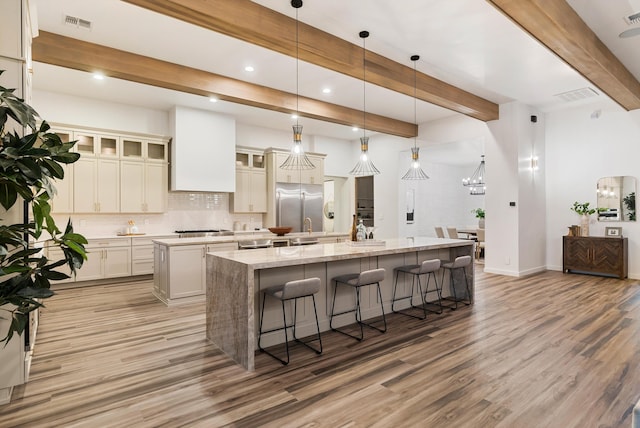 kitchen featuring light hardwood / wood-style floors, beam ceiling, an island with sink, and hanging light fixtures