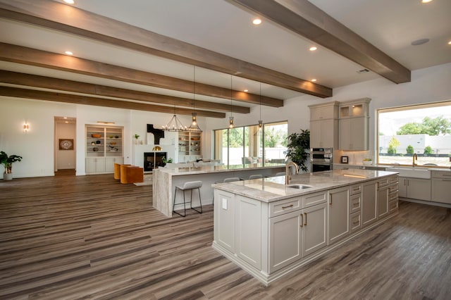 kitchen with light stone countertops, sink, a spacious island, beamed ceiling, and dark hardwood / wood-style floors