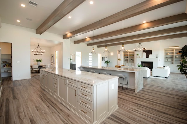 kitchen featuring a large island with sink, sink, pendant lighting, white cabinetry, and dark hardwood / wood-style flooring