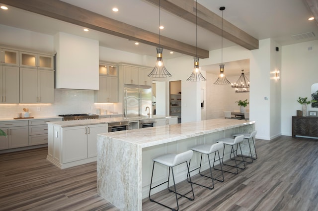 kitchen with a spacious island, beam ceiling, dark wood-type flooring, decorative light fixtures, and light stone counters