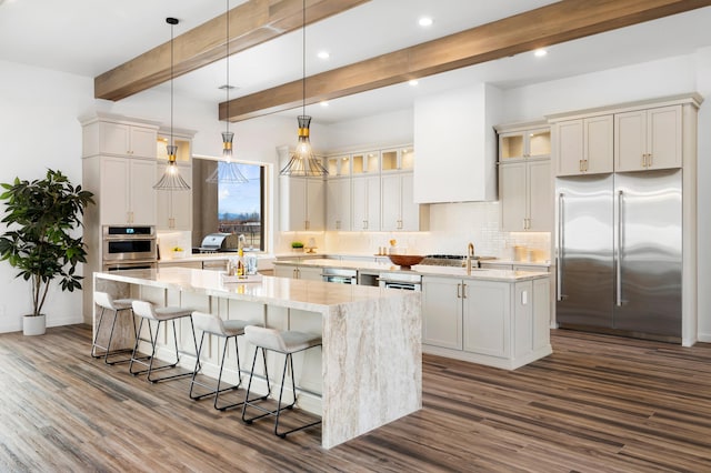 kitchen featuring beam ceiling, hanging light fixtures, an island with sink, dark hardwood / wood-style floors, and high quality fridge