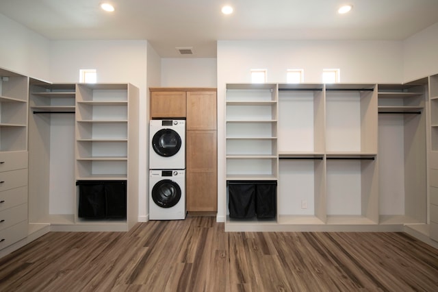 laundry room featuring dark wood-type flooring, stacked washer and dryer, and cabinets