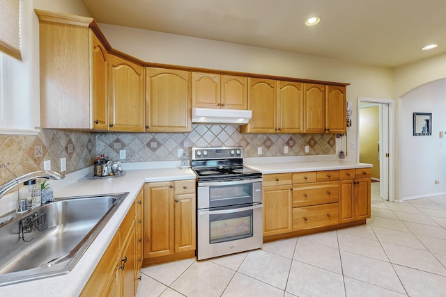 kitchen with range with two ovens, arched walkways, a sink, light countertops, and under cabinet range hood