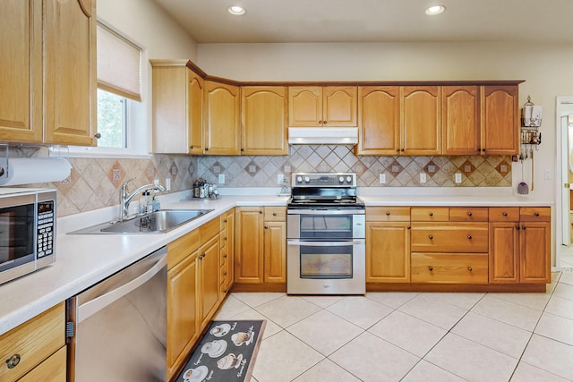 kitchen with under cabinet range hood, appliances with stainless steel finishes, light countertops, and a sink