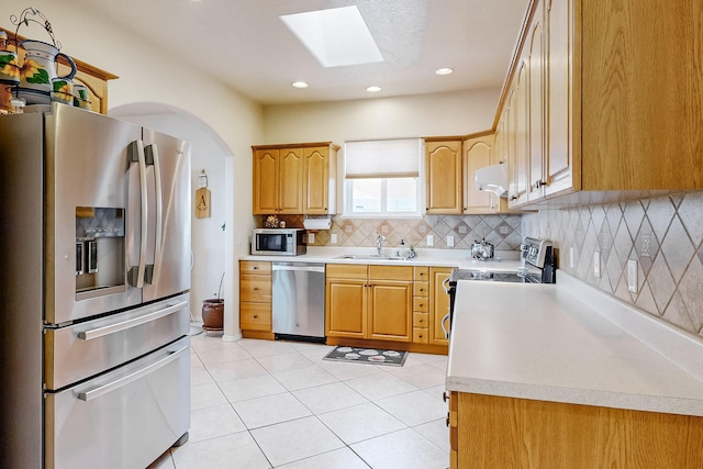 kitchen with tasteful backsplash, under cabinet range hood, light countertops, a skylight, and stainless steel appliances