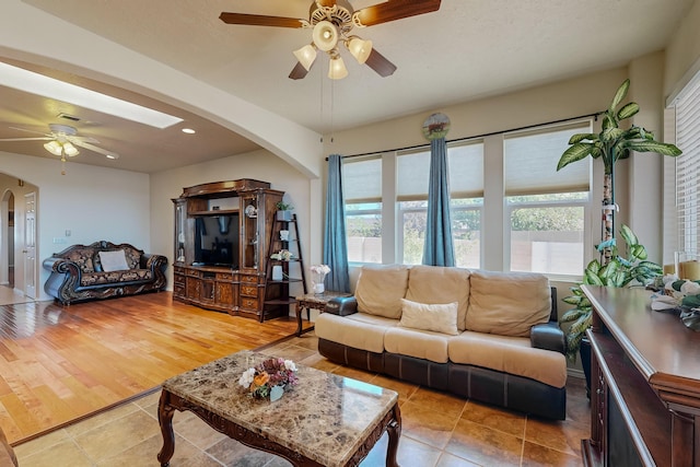 living area featuring arched walkways, a ceiling fan, a wealth of natural light, and light tile patterned flooring