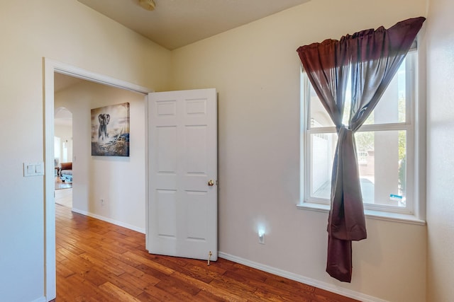 unfurnished room with arched walkways, baseboards, and wood finished floors