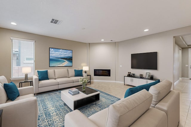 living room with light tile patterned floors, visible vents, baseboards, a glass covered fireplace, and recessed lighting